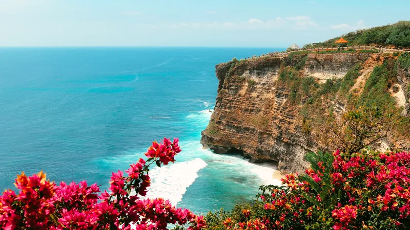 The cliffs below Uluwatu temple dropping into turquoise water, framed by flowers