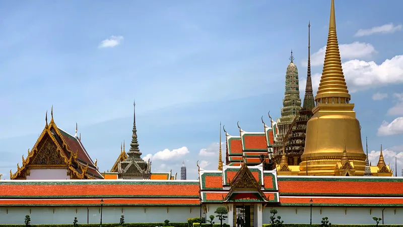 The golden spires and orange roofs of the Grand Palace against a blue sky