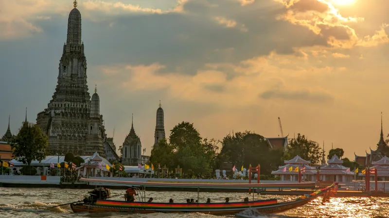 A long-tail boat passing Wat Arun on the Chao Phraya river in warm light