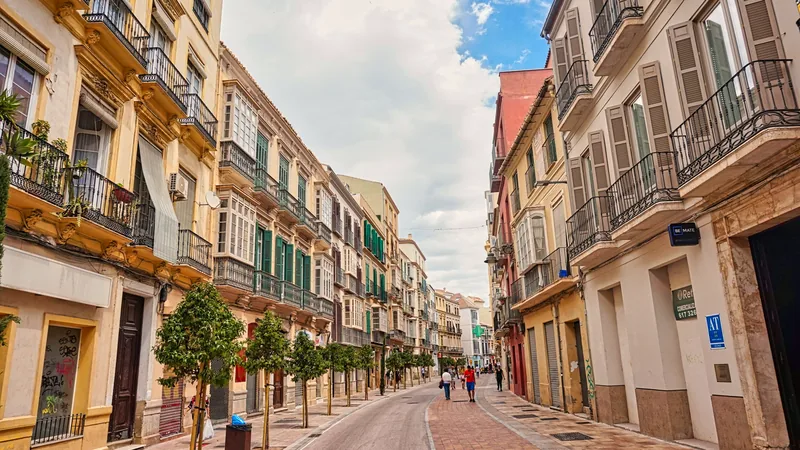 A narrow old-town street in Malaga with the cathedral tower beyond