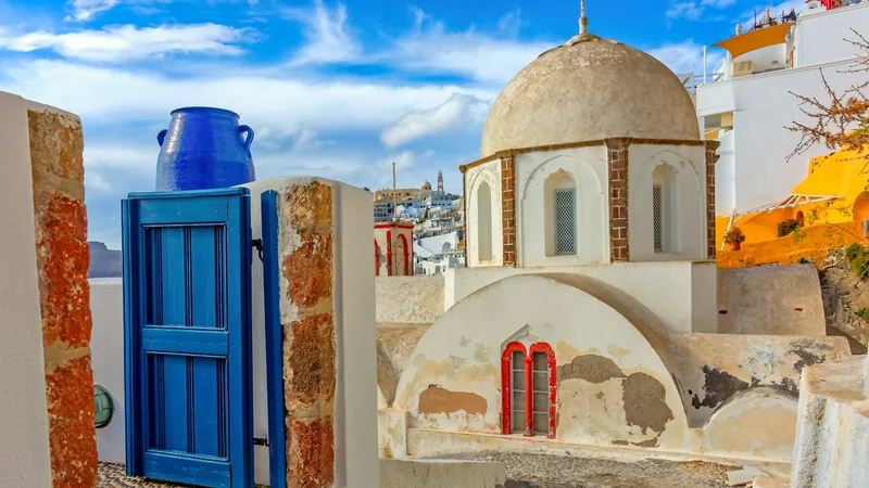 A blue gate and whitewashed dome in a Santorini village lane